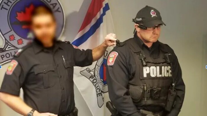 Un policier à la face floue montre une caméra d'intervention sur l'épaule de Michael Dimini. 