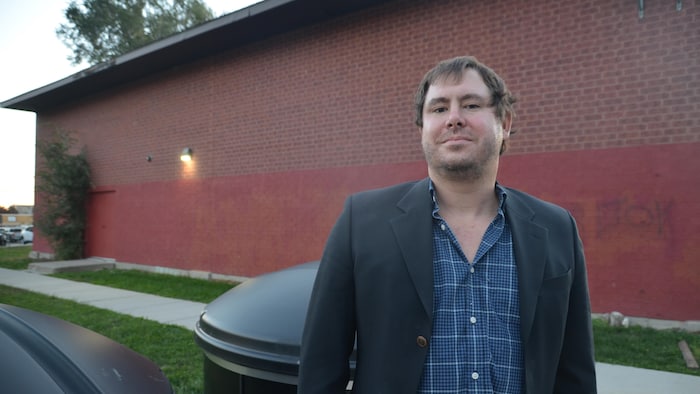 Un homme devant un édifice en brique, dehors.