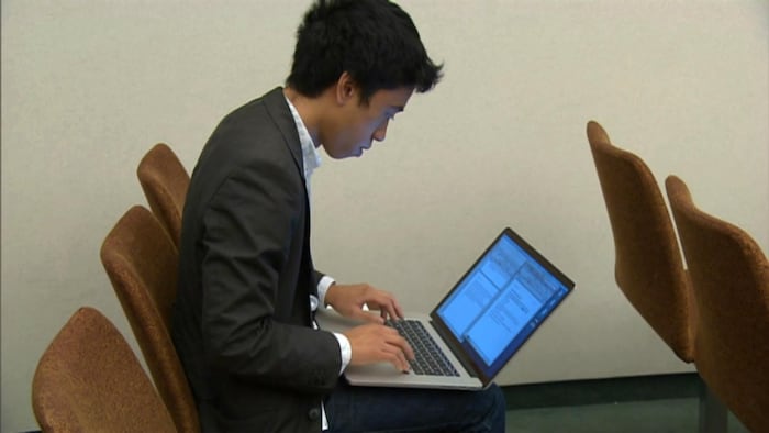 مايكل نْغُويِن جالس على كرسي ويعمل على حاسوبه المحمول.