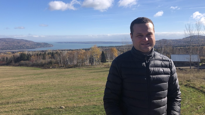 Un homme pose. Derrière lui on aperçoit le fleuve Saint-Laurent et L'Isle-aux-Coudres.