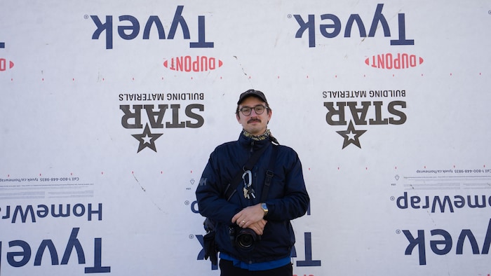 Un photographe debout contre un mur de membrane de construction blanche.