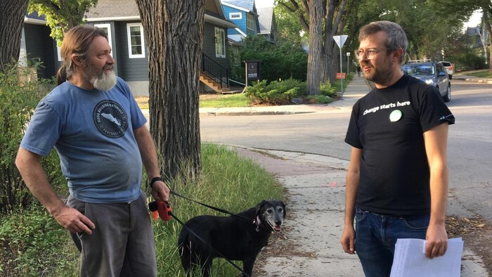 Le candidat du Parti vert Michael Wright discute avec l'un de ses concitoyens dans le district de Regina-Lewvan, en Saskatchewan. Le citoyen tient un chien en laisse.