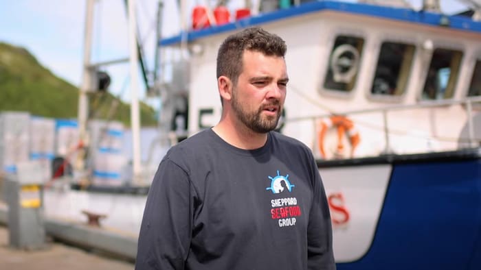 Un homme se tient debout devant un bateau de pêche.