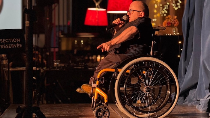 Un homme en fauteuil roulant avec un micro sur une scène.