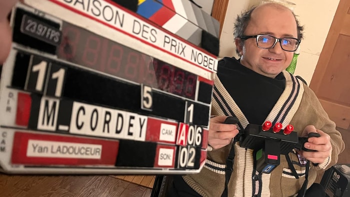 Michel Cordey en fauteuil roulant avec un clapet de cinéma.