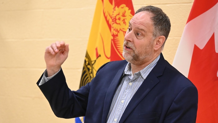 Michel Côté devant des drapeaux du Nouveau-Brunswick et du Canada.