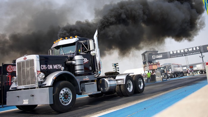 Un camion noir produisant une épaisse fumée noire lors d’une course.