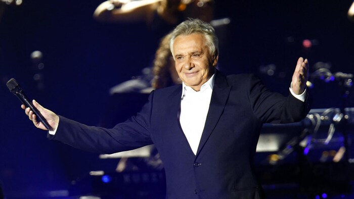 Le chanteur ouvre les bras sur scène avec un micro dans la main droite.