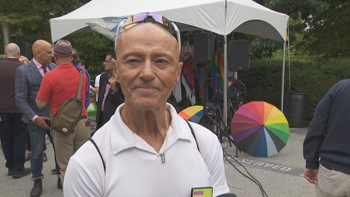 Michel Saint-Amant. Derrière lui, des parapluies avec les différentes couleurs de l'arc-en-ciel.
