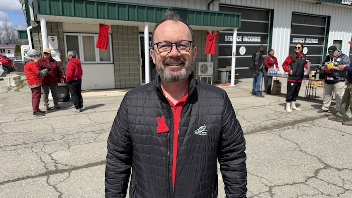 Michel Vaillant pose tout sourire devant le bureau municipal, après la marche. Il porte un chandail rouge sous son manteau et un écusson d'une robe rouge.