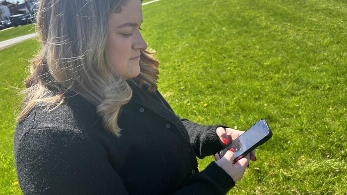 Une femme tenant son cellulaire dans ses mains.