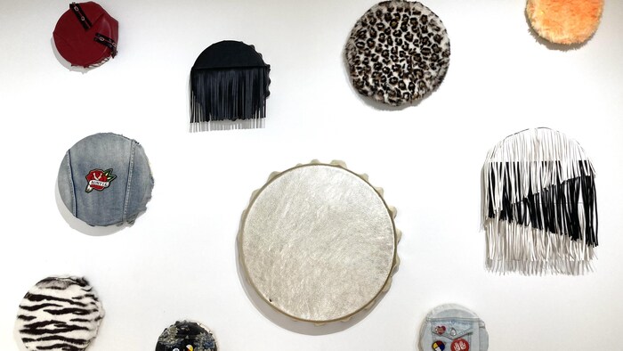 Des tambours aux matériaux variés sont exposés sur un mur de la galerie.