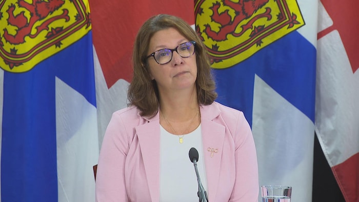 La ministre est assise devant les drapeaux de la Nouvelle-Écosse. Elle regarde la caméra.