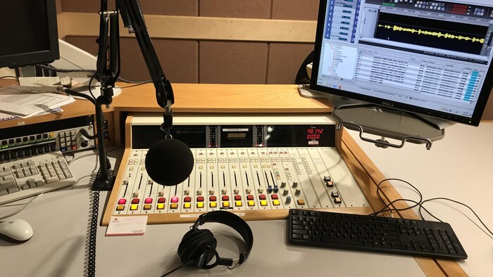 Un studio radio avec un microphone, un écran d'ordinateur et une console de mixage audio.