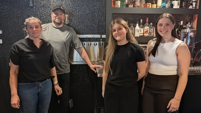 Trois femmes et un homme posent pour la photo devant un comptoir de boissons alcoolisées.   