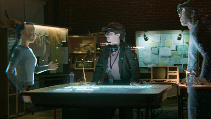 Deux hologrammes sont autour d'une table avec une personne portant un casque.