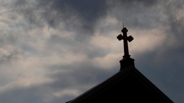 Des nuages noires se glissent à l'arrière-plan d'une croix sur le toit d'une église catholique de Pittsburgh.