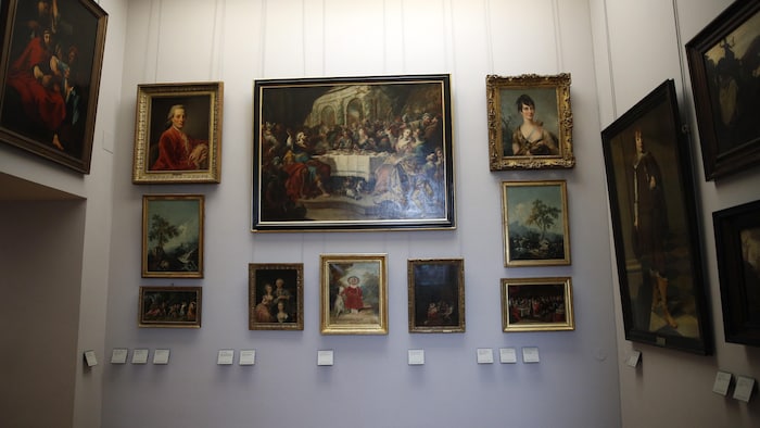 Plusieurs peintures de diverses tailles sont accrochées sur les murs d'une salle du musée du Louvre