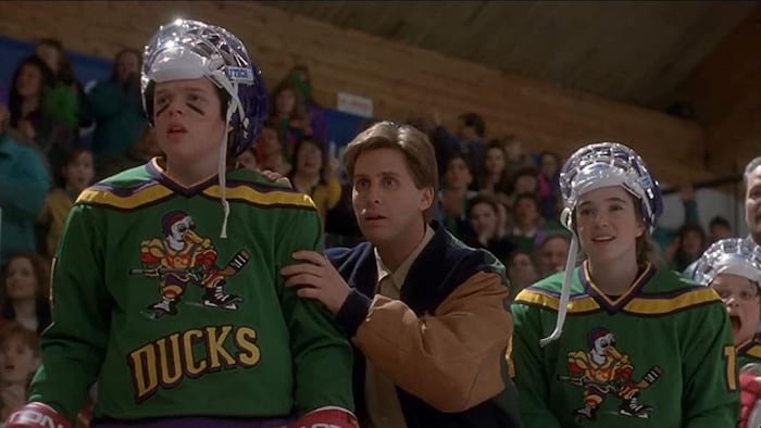 De jeunes joueurs de hockey, le casque relevé, regardent devant eux avec leur entraineur.