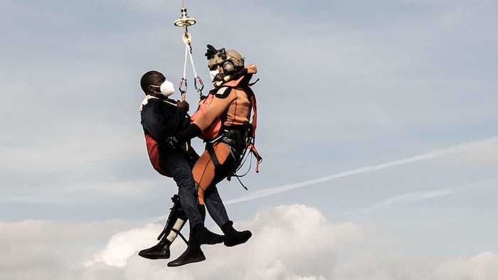 Un migrant aidé par un sauveteur de l'armée de l'air française. Tous deux sont suspendus à un câble.