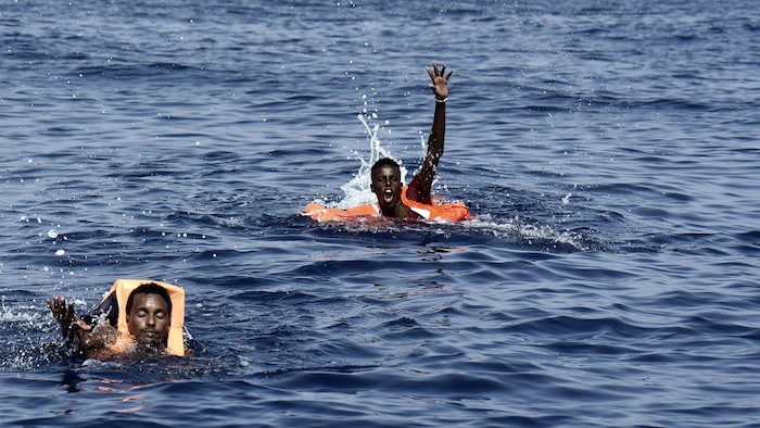 Deux hommes en mer, dont un lève la main appelant au secours.