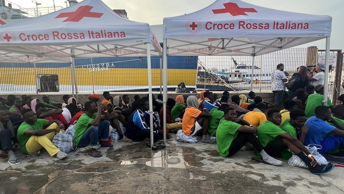 Des migrants assis sous des tentes de la Croix-Rouge italienne.