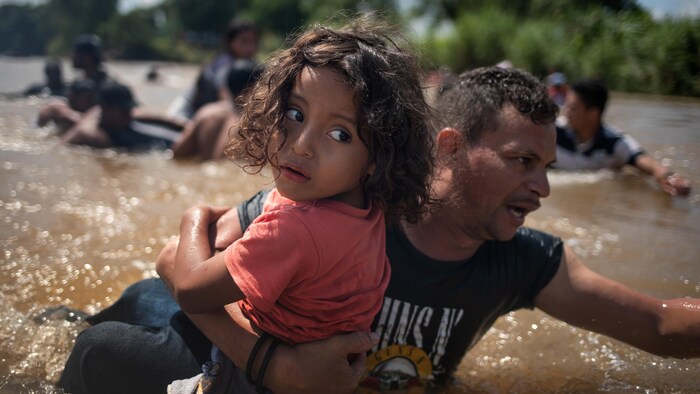 Un homme d’une caravane de migrants d'Amérique centrale en route vers les États-Unis, porte une jeune fille en traversant le fleuve Suchiate jusqu'au Mexique.