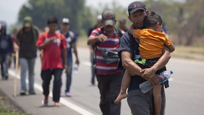 Un homme porte un enfant dans ses bras. Des hommes marchent aussi derrière.