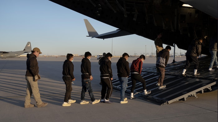 Des hommes enchaînés aux poings et aux chevilles font la file pour embarquer dans un avion.