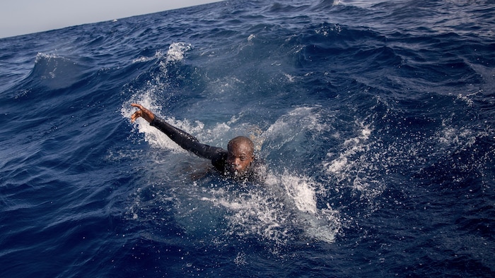 Un migrant, la tête sortie de l'eau, tend un bras. 