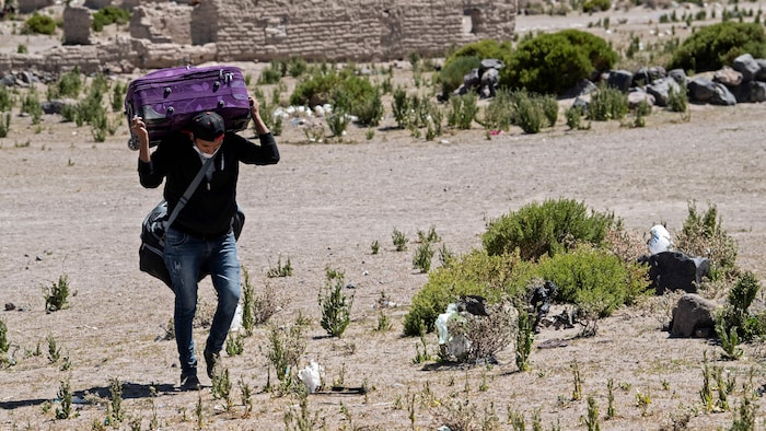 Un homme marche dans une zone désertique avec une valise sur les épaules.