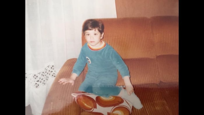 Un jeune Mikael Taieb est assis sur un divan.