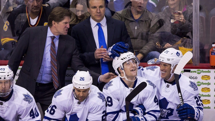 Les joueurs des Leafs célèbrent au banc. Derrière, Jim Hiller écrit sur carton à côté de Mike Babcock, qui parle aux joueurs.