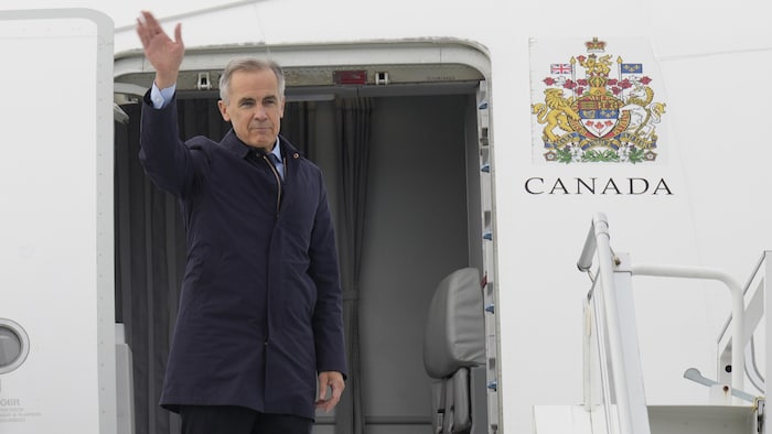 Mark Carney devant la porte d'un avion.