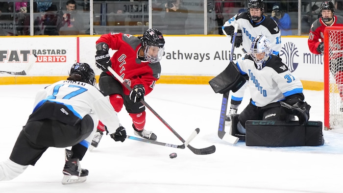 Une joueuse de hockey d'Ottawa au milieu de trois joueuses de Toronto pendant un match.