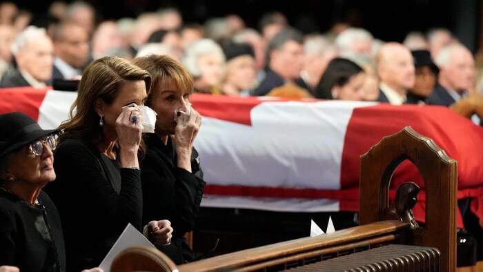 Deux femmes sèchent leurs larmes à côté d'un cercueil. 