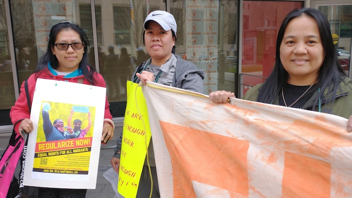 Trois femmes fixent l'appareil-photo, lors d'une manifestation pour les droits des migrants.