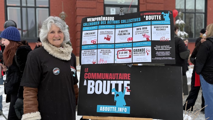 Lise Dion devant une pancarte « Le communautaire à boutte ».