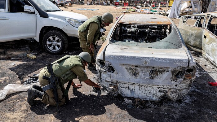 Des soldats examinent un véhicule qui a été incendié.
