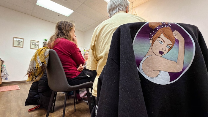 Des femmes assises de dos sur des chaises. Un chandail déposé sur une des chaises montre une femme qui contracte son biceps. 