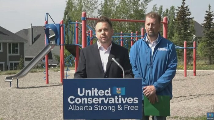 Nicholas Milliken et Mike Ellis, du Parti conservateur uni, derrière un lutrin dans un parc pour enfants.