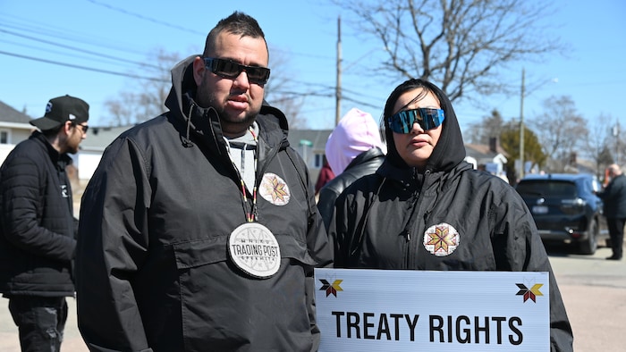 Adam et Mimi Jadis posent pour la photo. Mimi Jadis tient une pancarte sur laquelle il est écrit « Treaty rights are not crimes », c'est-à-dire « les droits issus des traités ne sont pas des crimes ». 