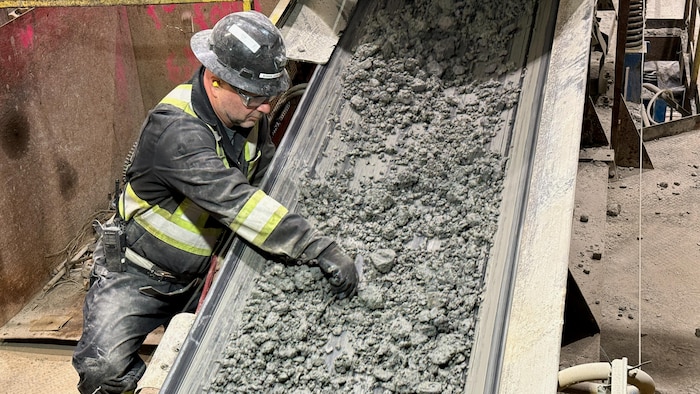 Un ouvrier retire des corps étrangers du minerai dans un convoyeur.