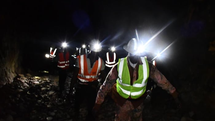 Une demi-douzaine de personnes avec des lampes frontales avancent dans une galerie de la mine. (16 avril 2022)