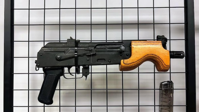 Un pistolet noir avec un garde-main en bois est attaché par des attaches autobloquantes à une grille métallique noire. 