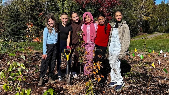 Six jeunes filles debout derrière un des petits arbres qu'elles viennent de planter.