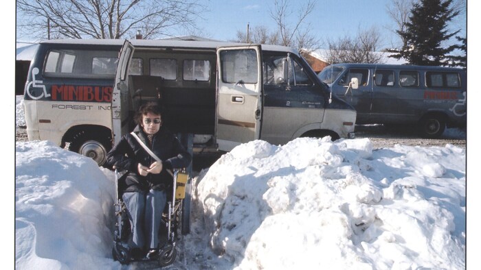 Jacques Forest en fauteuil roulant dans la neige, devant deux minibus Forest.