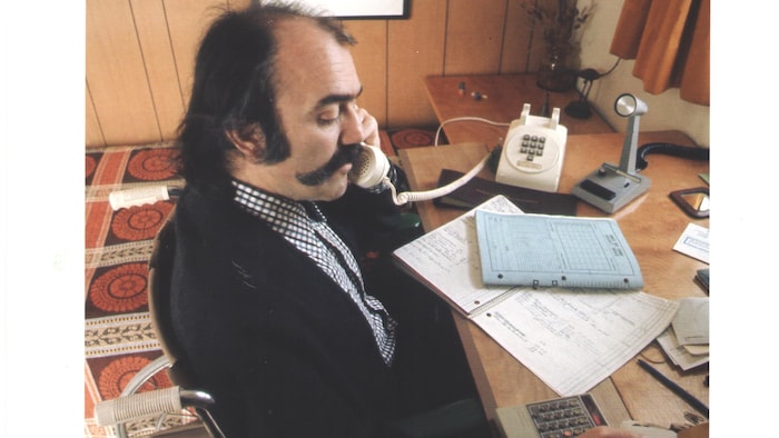Jean-Marc Forest en fauteuil roulant à son bureau est au téléphone.