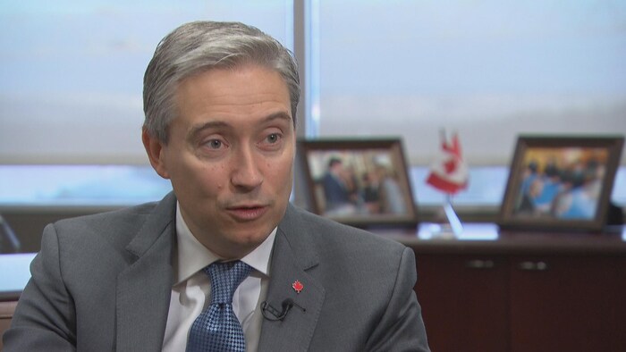 Le ministre des Affaires étrangères François-Philippe Champagne assis à un bureau avec des photos et des petits drapeaux canadiens derrière lui. 