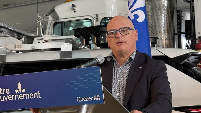 Jonatan Julien prononce une allocution derrière un pupitre, devant un camion. 